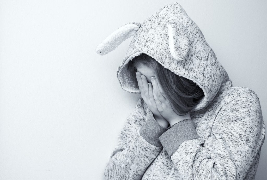 A youth in a hoodie hides her face out of anxiety